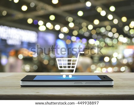 Shopping cart icon on modern smart phone screen on wooden table in front of blur light and shadow of shopping mall, Shop online concept Royalty-Free Stock Photo #449938897