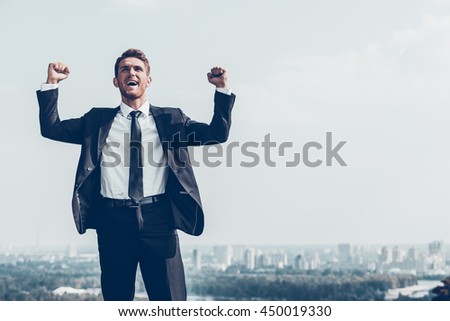 Used to win every day. Happy young man in formalwear keeping arms raised and expressing positivity while standing outdoors with cityscape in the background Royalty-Free Stock Photo #450019330