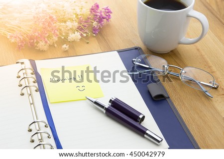 A cup of coffee and opened notebook with MORNING message on wooden background with pen, glasses and flowers. warm tone. MORNING message on wooden background with pen, glasses and flowers. warm tone.