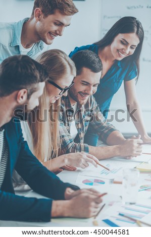 Business team at work. Side view of five cheerful business people in smart casual wear discussing something while looking at the graphs and charts Royalty-Free Stock Photo #450044581