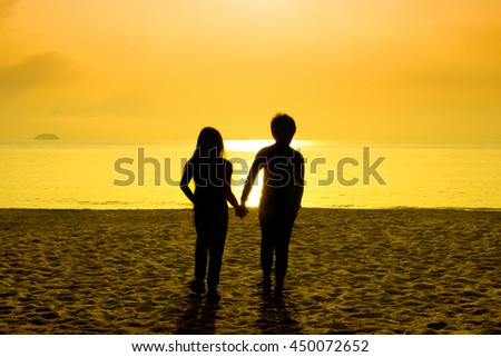 Silhouette picture of male and female children holding hands on a beach during orange tinted sunrise / sunset