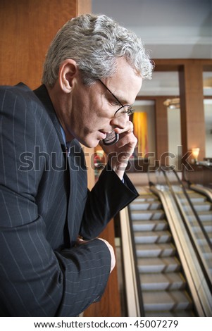 Businessman on his cellphone looking over the railing.  Escalators run in the background. Vertical shot.