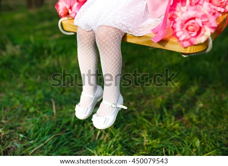 Little girl riding on a swing. legs close up on a background of green grass.