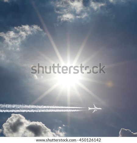 An airplane creating jet stream trail across a bright shining sun.
