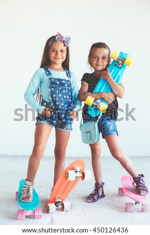 Two 7 years old children wearing cool fashion jeans clothing posing with colorful skateboard in white studio, urban style