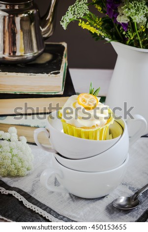 Cupcakes with cream cheese in white up. Jar, books and spoon on wooden table. Selective focus.