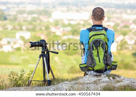 Hiker photographer  sitting on a rock looking forward near a camera on a tripod