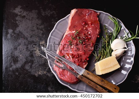 Raw fresh meat Striploin steak and seasoning on a grey vintage plate over dark metal background, top view