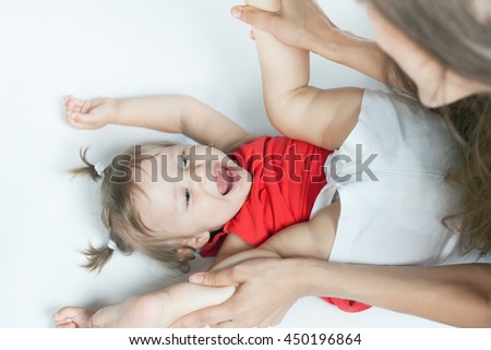 Funny baby girl doing exercise and yoga with her happy mother on a white bed. Newborn looking at the camera and smiling. Mothercare is most important in baby life