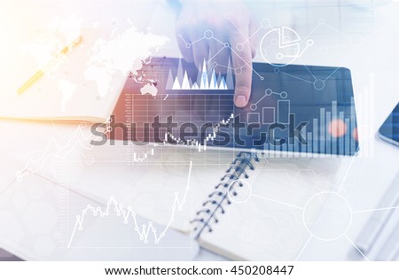 Closeup of male hand using tablet with abstract business charts and graphs on office desktop with various items. Toned image