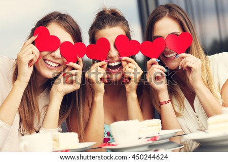 Picture presenting three girlfriends holding hearts in cafe