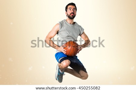 Man playing basketball jumping over ocher background
