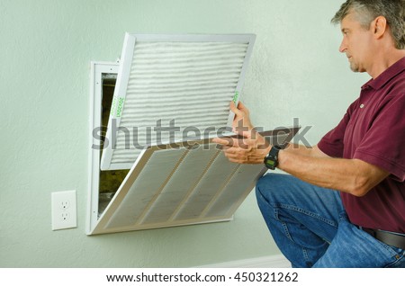 Professional repair service man or diy home owner installing a clean new air filter on a house air conditioner which is an important part of preventive maintenance. Royalty-Free Stock Photo #450321262