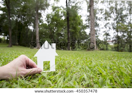 Hand holding house against green field