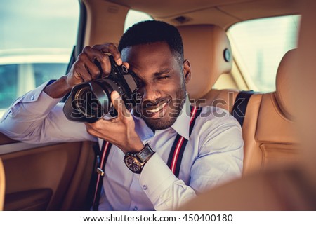 African american male in a white shirt shooting with dslr camera from car's back seat.