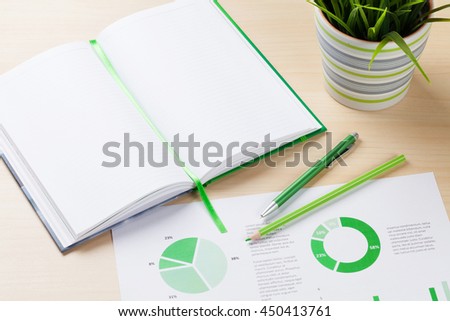 Office desk workplace with charts, plant and notepad on wooden table