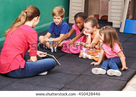 Group of kids talking about book with nursery teacher in preschool