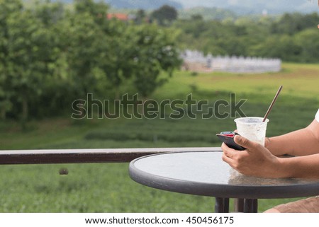Asian adult man in white T-shirt operate small smart phone in beautiful nature with plastic cup