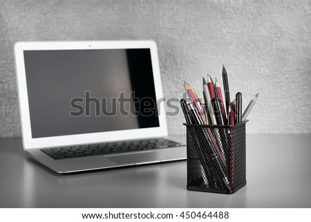 Pencils and pens in metal holder with laptop  on grey wall background