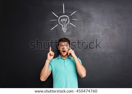 Amazed young man talking on cell phone and having an idea over blackboard background