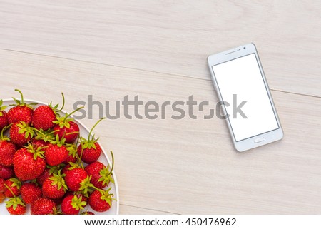 Fresh natural summer strawberries on a plate and a gadget smartphone with white screen blank for design on white wooden table background. Mockup template for Breakfast and dessert. Top view flat lay