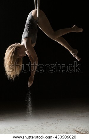 Acrobatic woman hunging on aerial hoop and pouring flour