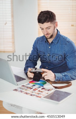 Photographer checking photos in camera at desk in office