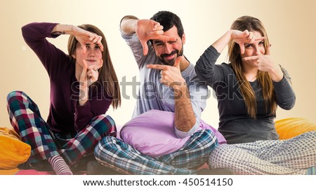 Three friends on a bed focusing with his fingers over ocher background
