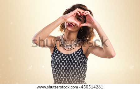Pretty girl making a heart with her hands over ocher background