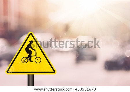 Bicycle warning sign on blur traffic road with colorful bokeh light abstract background. Copy space of transportation and travel concept. Retro tone filter color style.