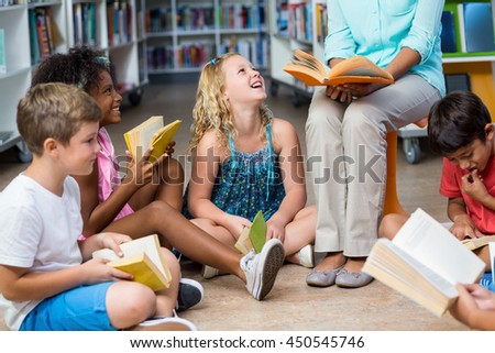 Low section of female teacher with smiling children reading books in library