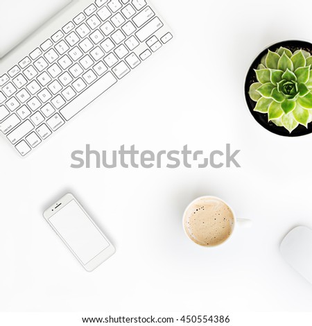 White office desk table with wireless aluminum keyboard, cup of coffee, smart phone in iphon style with blank screen, mouse and succulent flower in pot. Top view with copy space. Flat lay.  Royalty-Free Stock Photo #450554386