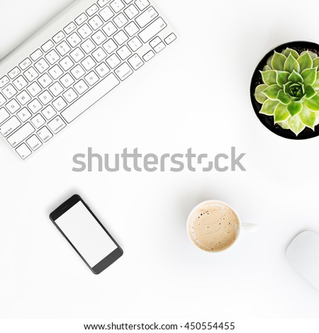 White office desk table with wireless aluminum keyboard, cup of coffee, smart phone in iphon style with blank screen, mouse and succulent flower in pot. Top view with copy space. Flat lay.  Royalty-Free Stock Photo #450554455