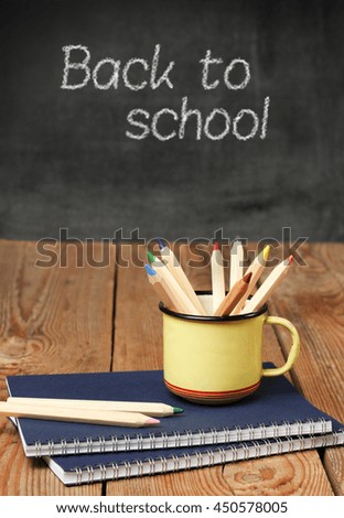 Still life, business, education concept. Pencils in a mug and notebook on a wooden table with chalkboard. Selective focus, copy space background