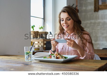 Young woman photographing her meal in restaurant Royalty-Free Stock Photo #450580336