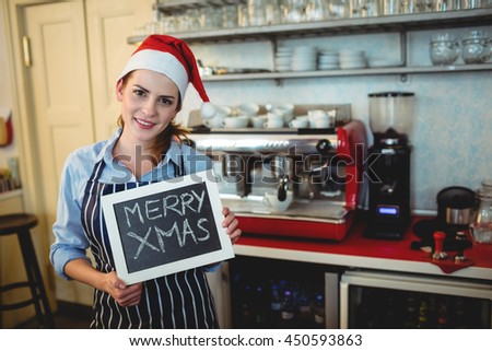 Portrait of young barista holding Christmas sign on blackboard at cafe
