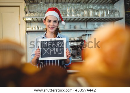 Portrait of happy young barista holding Christmas on blackboard at cafe