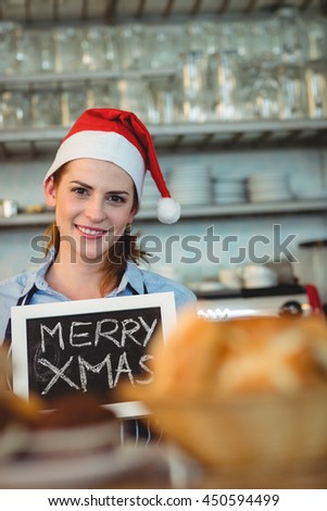 Portrait of happy young barista holding blackboard with Christmas text at cafe