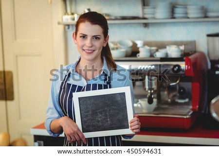 Portrait of happy young female barista holding blank chalkboard at cafe
