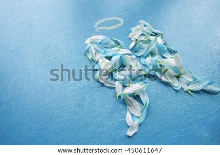 White and blue flower petals arranged on a wooden surface in the form of wings with painted halo.