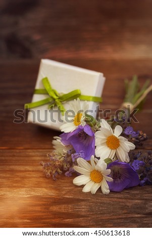 Bouquet of flowers with small gift on wooden background