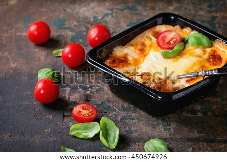 Cooked meat lasagna in black plastic box, served with vintage fork,  fresh cherry tomatoes and basil leaves over old dark wooden textured background. Market semi-finished theme. Royalty-Free Stock Photo #450674926
