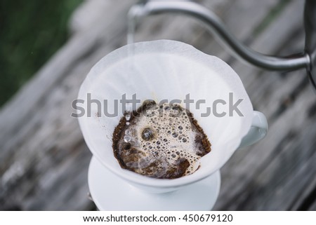 Delicious pourover coffee blossoming while man pours water into the dripper on the ground coffee beans. Summer picnic on the old wooden table background Royalty-Free Stock Photo #450679120