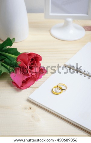 Two gold wedding ring of two persons on notebook with pink rose