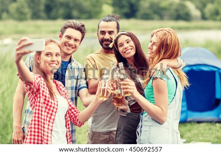 camping, travel, tourism, hike and people concept - happy friends with glass bottles drinking cider or beer and taking selfie by smartphone at camping