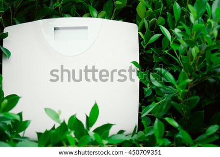 Digital weight scale on green leaves background.