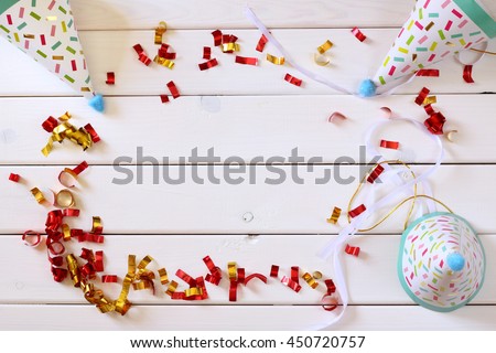 Party hat next to colorful confetti on wooden table. Top view
