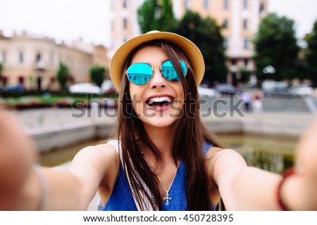 Young girl take selfie from hands with phone on summer city street. Urban life concept. Royalty-Free Stock Photo #450728395