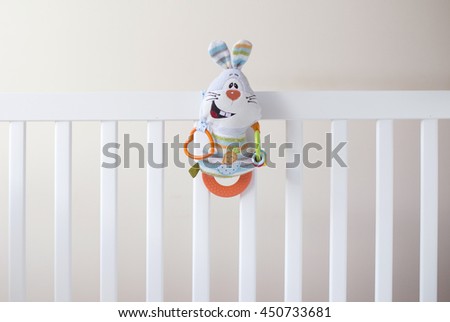 One soft colorful rabbit toy at white children's bed.