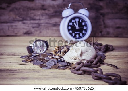white skull  model on stack of coins with old rusty metal chain, man watch, dry roses  and alarm clock on wooden background, Vignette, concept